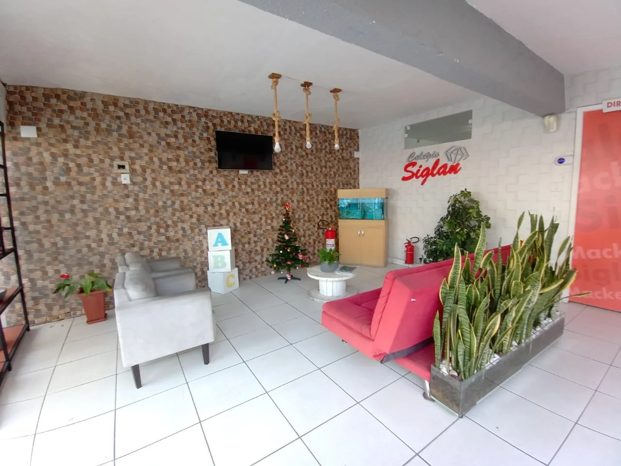 Recepção do Colégio Siglan em Perus com identidade visual vermelha, poltronas e plantas