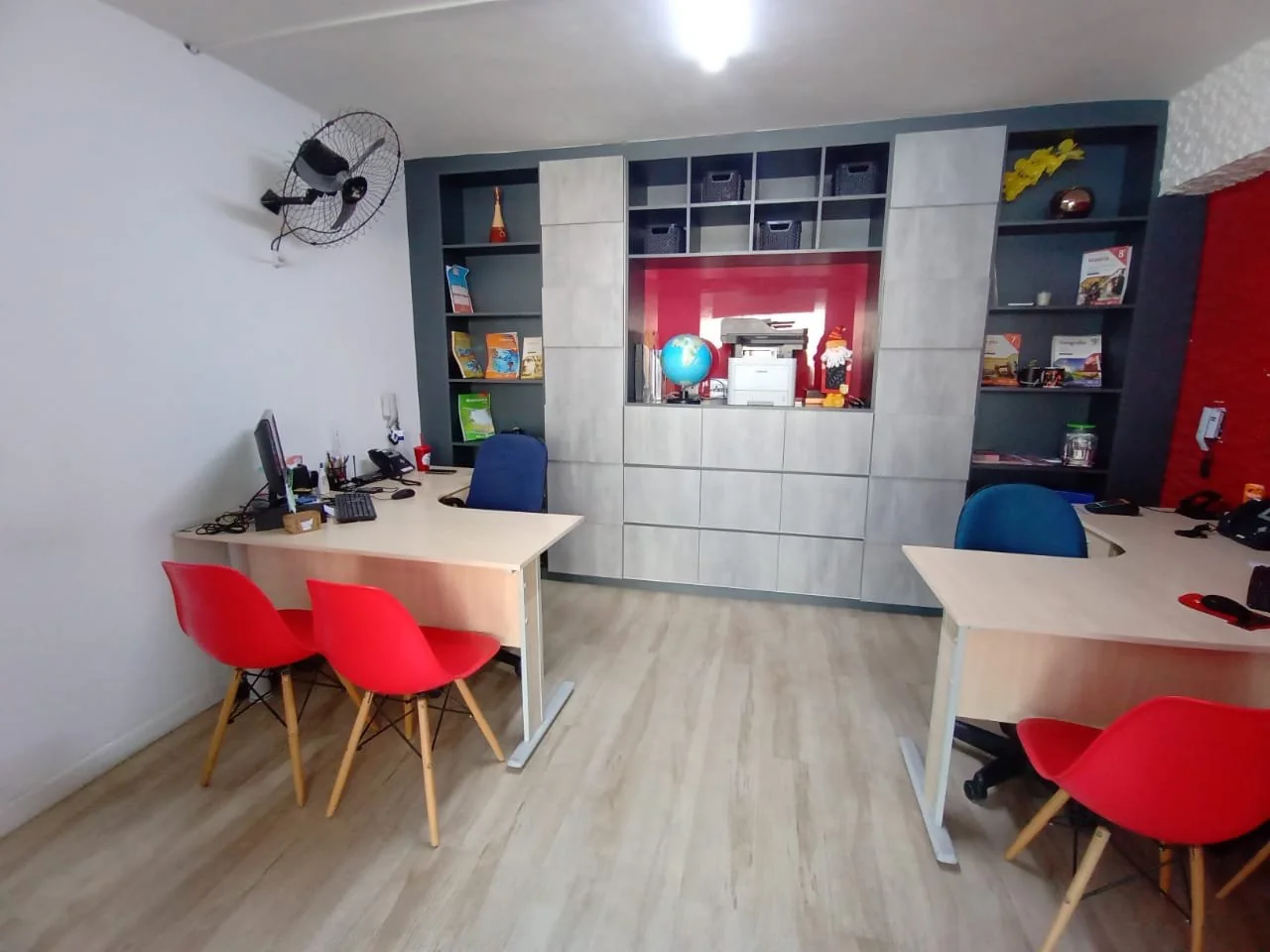 Ambiente de atendimento do Colégio Siglan em Perus com mesas, cadeiras vermelhas e materiais escolares